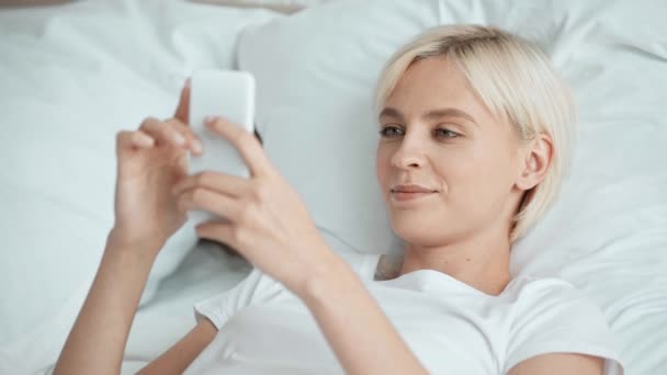 Pijama Güzel Kız Akıllı Telefon Kullanarak Yatakta Gülümseyen — Stok video