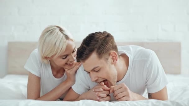 美丽的微笑夫妇手牵手 男人咬手和亲吻在床上的女人 — 图库视频影像