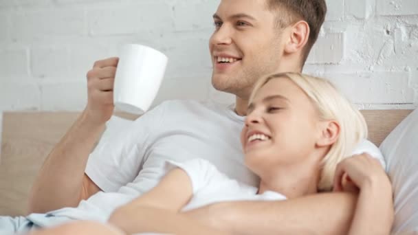 美しいカップルが微笑み 抱きしめてベッドで話し コーヒーを飲む男 — ストック動画