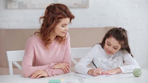 Usmívající Matka Pomáhající Dceři Domácím Úkolem Zatímco Píše Knize Kopií — Stock video