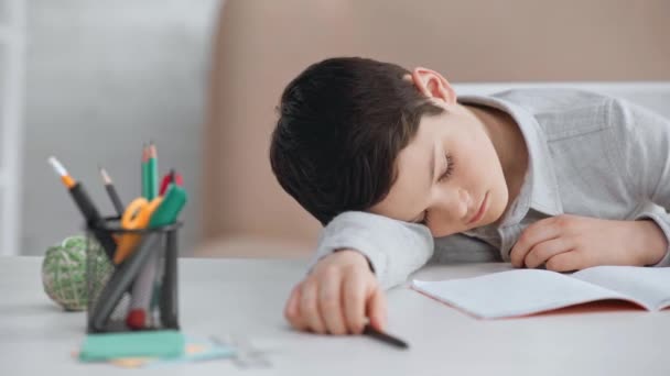 コピーブック 鉛筆の近くで机の上で眠っているペンを持つ疲れた十代の男子学生 — ストック動画