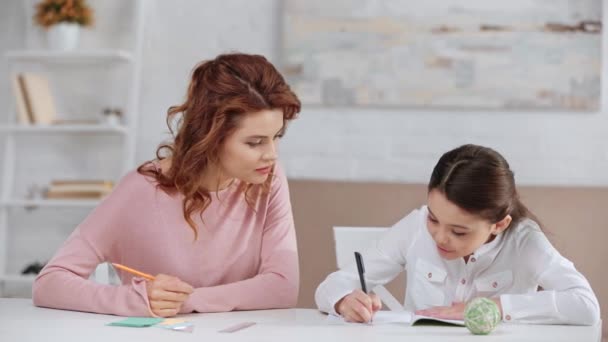 Madre Sosteniendo Lápiz Ayudando Hija Con Tarea Mientras Escribe Libro — Vídeos de Stock