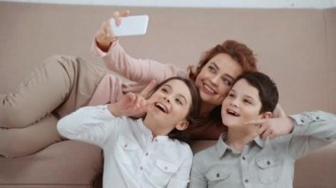 Kiev, Ukrayna - 15 Nisan 2019: Joystick'li iki çocuk, anne selfie çekerken barış işaretleri ve başparmaklarını yukarı yaslıyor