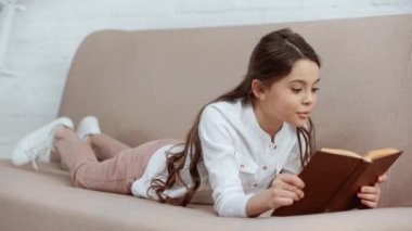 preteen çocuk kitap okuma, şaşkınlık ifade ve evde kanepeüzerinde yatarken gülümseyerek