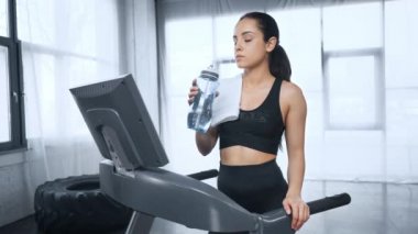koşu bandı içme suyu üzerinde güzel sporcu, kamera bakıyor ve spor salonunda gülümsüyor