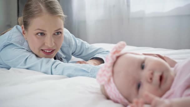 ベッドの上で幼児の近くでジェスチャー幸せな母親のラックフォーカス — ストック動画