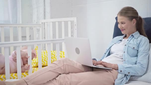 Madre Escribiendo Ordenador Portátil Cerca Hija Cuna — Vídeos de Stock