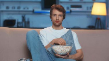 oturma odasında tv izlerken patlamış mısır yiyen üzgün adam