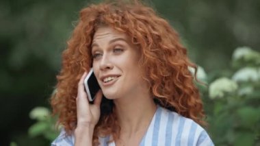 parkta akıllı telefon konuşurken mutlu kızıl saçlı kadın 