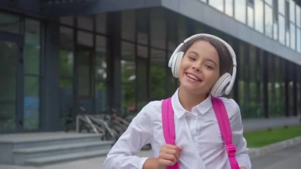 校庭でヘッドフォンで音楽を聴く幸せな女子高生 — ストック動画
