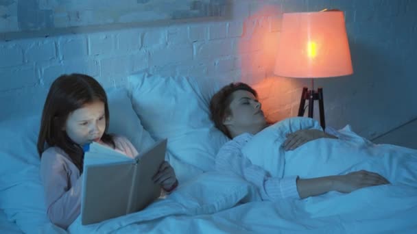 ベッドで懐中電灯付きの母睡眠と娘読書本 — ストック動画