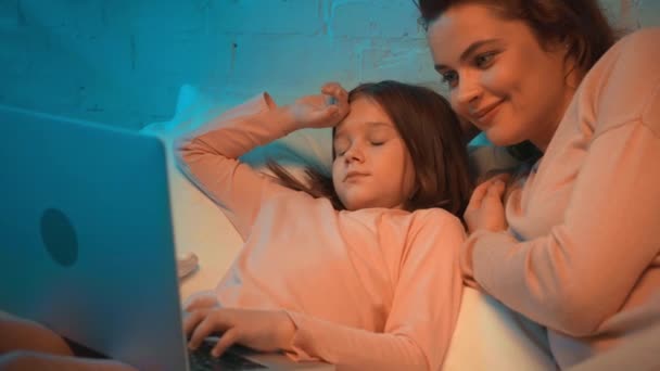 母亲和女儿在晚上在床上使用笔记本电脑 — 图库视频影像