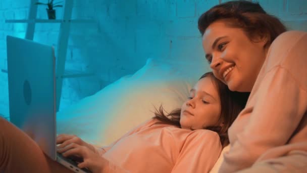 母亲和女儿使用笔记本电脑和笑在床上在晚上 — 图库视频影像