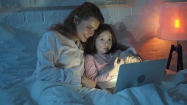yatakta dizüstü bilgisayarda film izlerken oyuncak ayı ile anne ve kızı