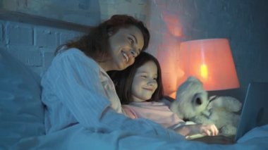 yatakta film izlerken oyuncak ayı ile mutlu anne ve kızı
