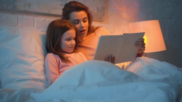 母と娘は夜ベッドで一緒に本を読む — ストック動画