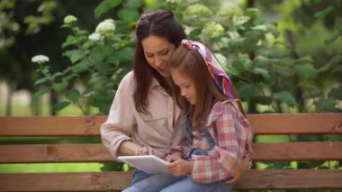 mutlu anne ve kızı parkta dijital tablet üzerinde oynarken