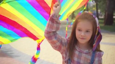 parkta gökkuşağı uçurtma ile yürüyen gülümseyen çocuk