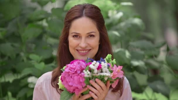 公園で花の匂いを嗅ぐ笑顔の女性 — ストック動画