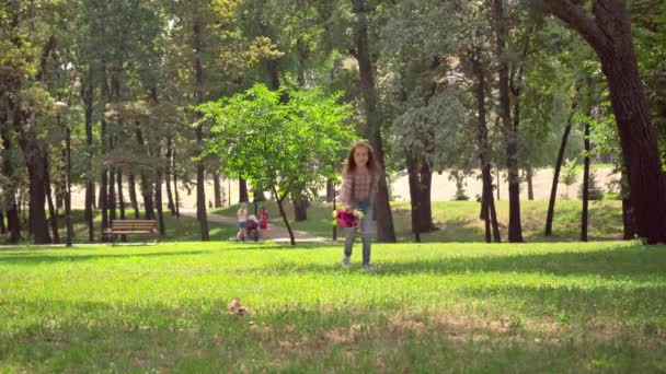緑の日当たりの良い公園で花と一緒に走っている赤毛の子供 — ストック動画