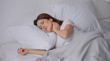 yatakta uyuyan ve boyun ağrısı çeken kadın