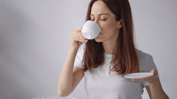 幸せな女性はベッドでコーヒーの匂いと飲み物を飲む — ストック動画