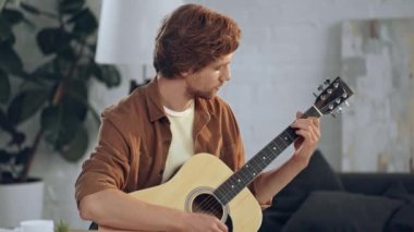 evde akustik gitar çalan genç konsantre adam