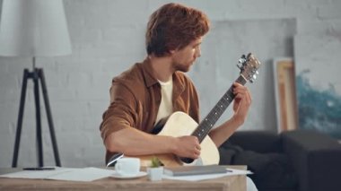 oturma odasında akustik gitar çalan genç kızıl saçlı adam