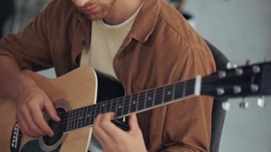 evde akustik gitar çalan genç adamın kısmi görünümü