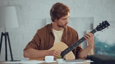 evde akustik gitar çalan odaklanmış kızıl saçlı adam