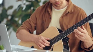 akustik gitar çalan ve dizüstü bilgisayar kullanan adamın kısmi görünümü