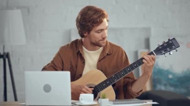 dizüstü bilgisayarda görüntülü sohbet sırasında akustik gitar çalan müzisyen