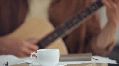 kahve fincanı yakınında akustik gitar çalan adamın seçici odak noktası