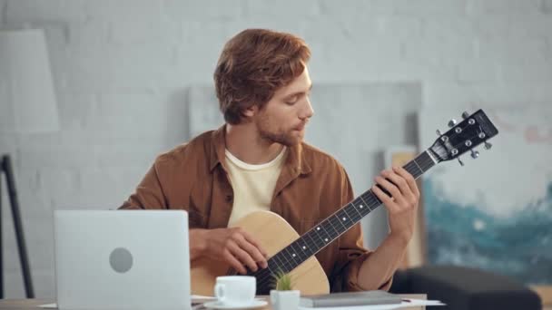 Pensativo Ruiva Homem Tocando Guitarra Acústica Perto Laptop — Vídeo de Stock