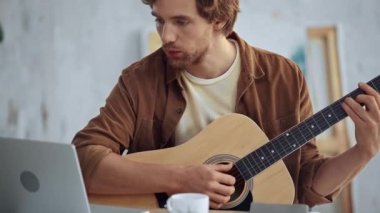 bilgisayar ekranına bakarken akustik gitar çalan ve şarkı söyleyen adam