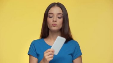 Düşünceli ve endişeli kız sarı üzerine izole akıllı telefon kullanıyor.