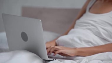 Yatakta oturan ve dizüstü bilgisayar kullanan kadın görüntüsü.