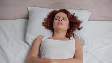 Karın ağrısı çeken ve yatakta hap alan üzgün bir kadın.