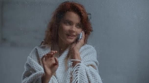 Uśmiechnięta Kobieta Rozmawiająca Smartfonie Przy Szklanym Oknie Kroplami Deszczu — Wideo stockowe