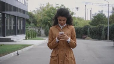 Gülümseyen Afrikalı Amerikalı kadın sokakta akıllı telefon kullanıyor. 