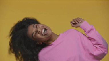 Mutlu Afro-Amerikalı kız pembe kazaklı, sarı saçlarını dalgalandırıyor.