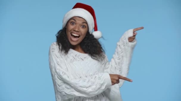 サンタの幸せなアフリカ系アメリカ人女性の帽子を指します指で青に隔離された — ストック動画