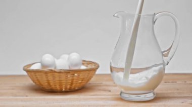Gri renkte izole edilmiş ahşap yüzeyde yumurtaların yakınındaki süte yavaş yavaş süt dökülüyor. 