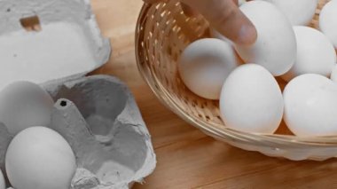 Hasır sepetin içine yumurtalarını koyan ahşap yüzeye bakan insan görüntüsü.