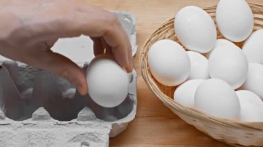 Hasır sepetten yumurtaları tahta yüzeyde kutuya koyan insan görüntüsü.