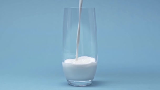 Αργή Κίνηση Του Γάλακτος Χύνοντας Γυαλί Μπλε Επιφάνεια — Αρχείο Βίντεο