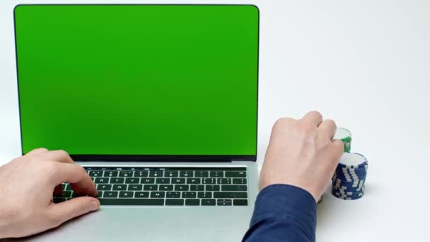 緑の画面を持つラップトップの近くの男のクロップドビュー白にポーカートークンを保持 — ストック動画