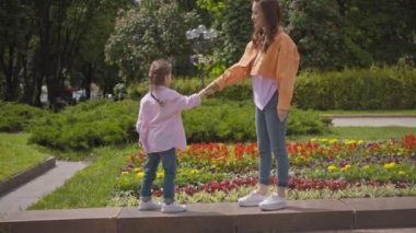 Anne ve kızı el sıkışıyor ve dışarıda çiçek tarhında sarılıyorlar.