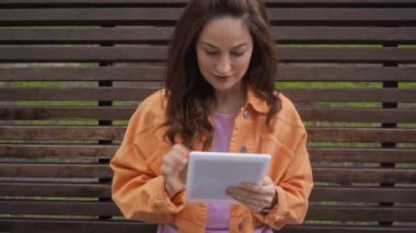 Mutlu kadın bankta otururken dijital tablet kullanıyor 