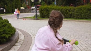 Mutlu çocuk parkta annesinin yanında scooter sürüyor. 